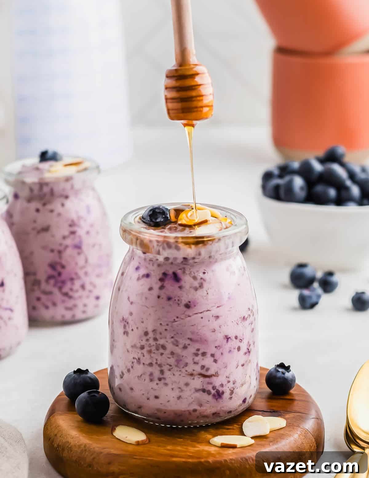Berry Burst Chia Delight 7 A jar filled with blueberry chia pudding topped with honey and blueberries. Other jars and bowls of blueberries are in the background.