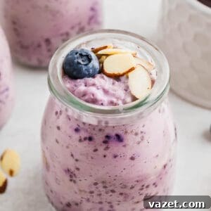 A glass jar filled with blueberry chia pudding topped with sliced almonds and a whole blueberry. Other jars of similar pudding are visible in the background.