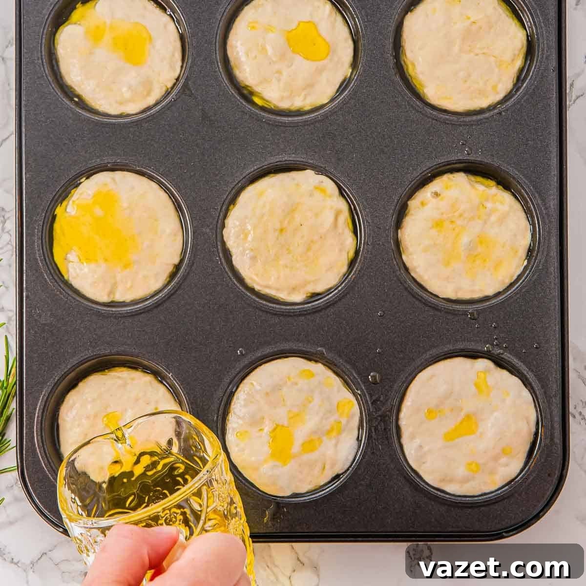 Drizzling olive oil on unbaked focaccia muffin batter.