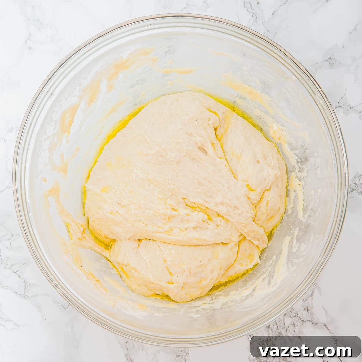 Risen, sticky focaccia dough in a glass bowl.