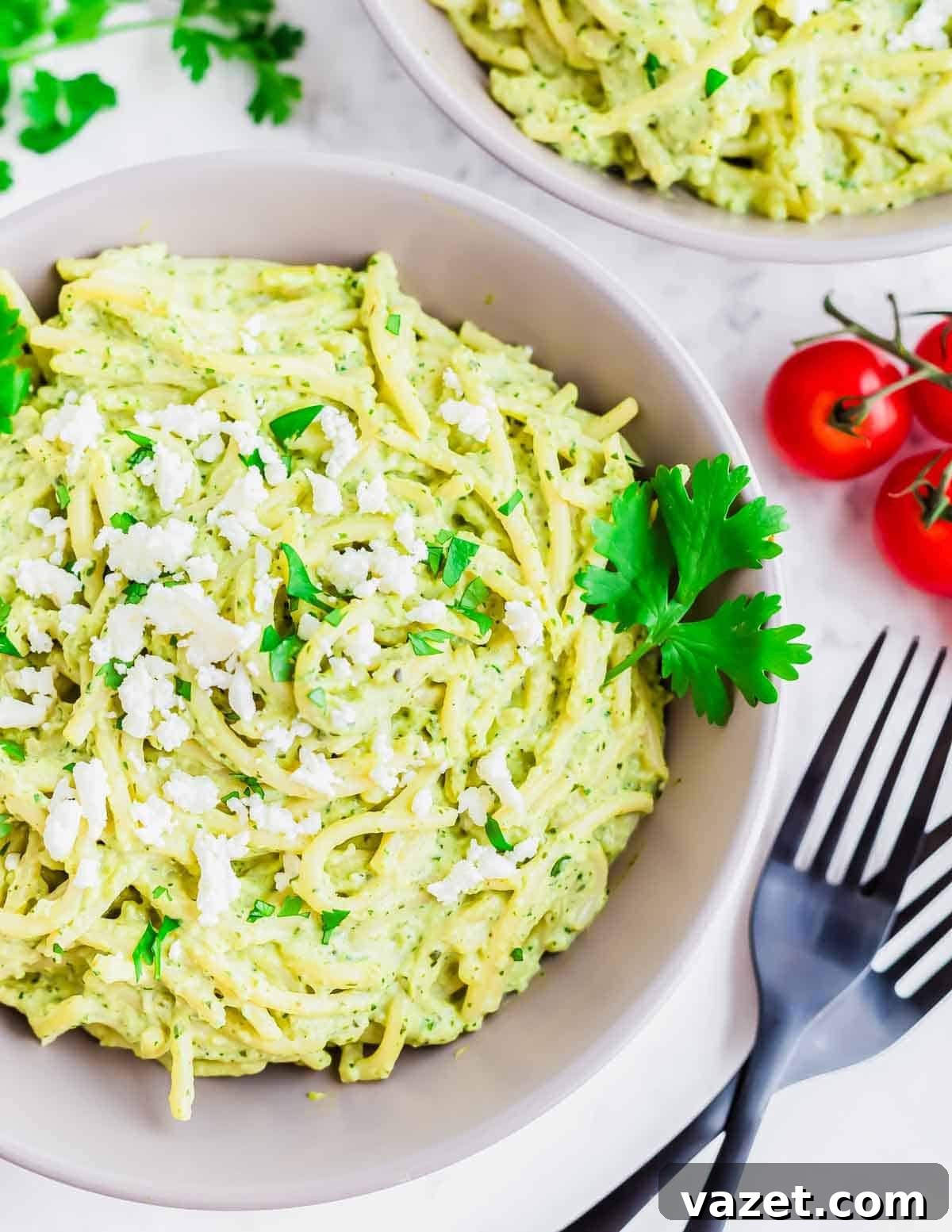 A delicious bowl of Espagueti Verde, creamy green pasta garnished with crumbled white cheese and fresh parsley, along with fresh parsley and tomatoes, ready to be enjoyed.