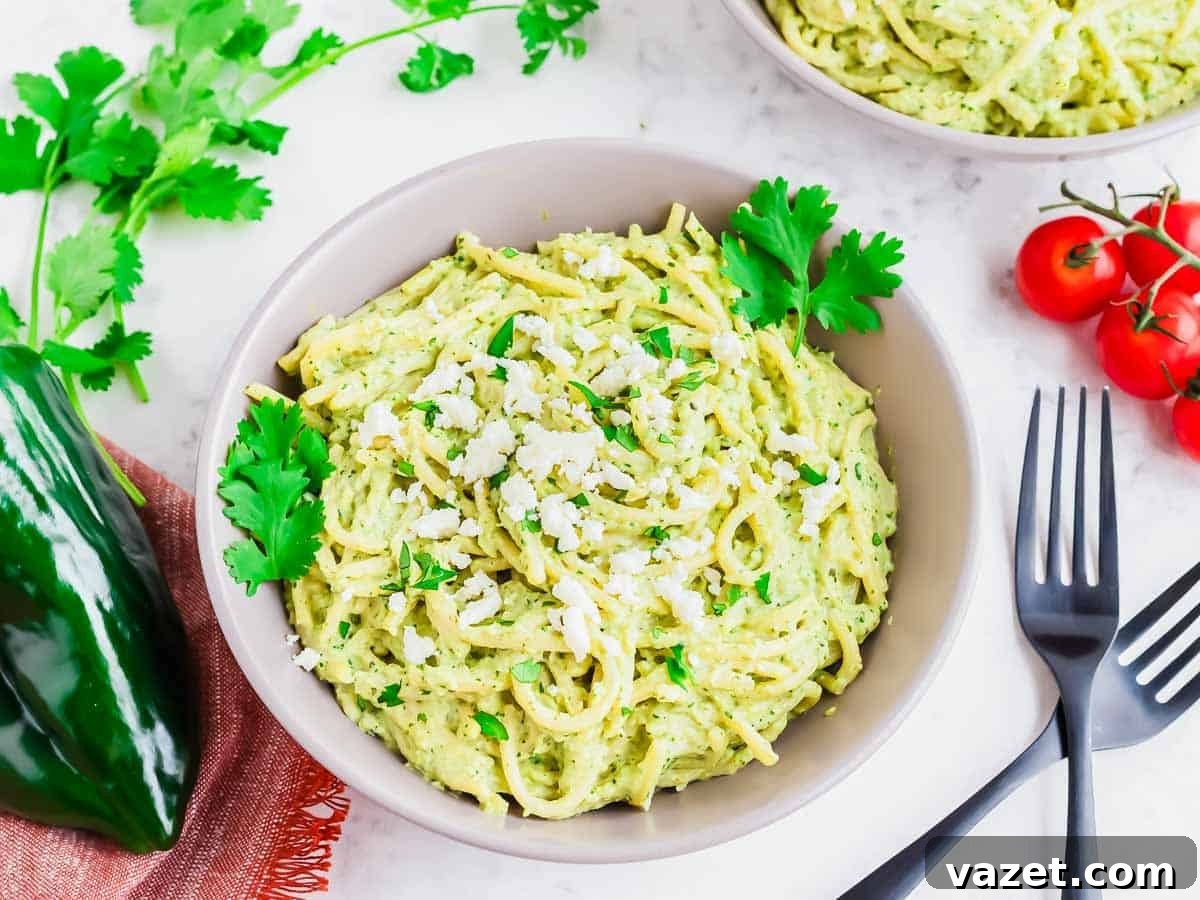 A beautifully styled bowl of Espagueti Verde garnished with cheese and cilantro, surrounded by other ingredients like cherry tomatoes and poblano pepper.