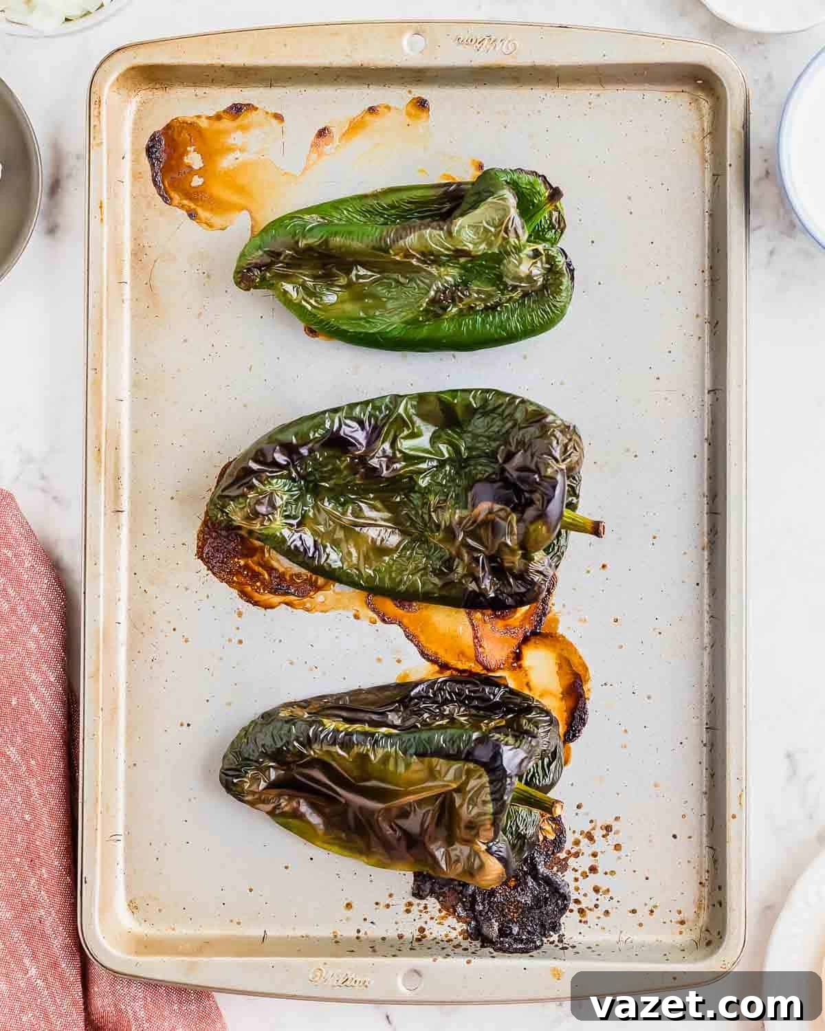 A baking sheet filled with perfectly roasted poblano peppers, charred and ready to add smoky flavor to the sauce.