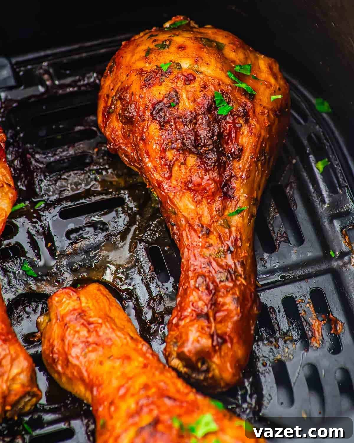 Close-up of a crispy, golden-brown roasted chicken leg in an air fryer basket, garnished with chopped parsley.