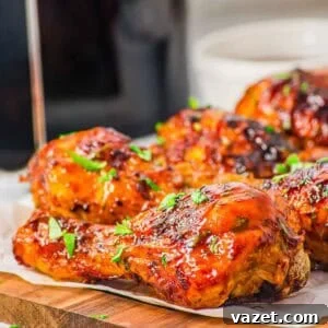 Close-up of BBQ glazed, air fryer chicken drumsticks garnished with chopped fresh herbs, arranged on a wooden board lined with parchment paper. The chicken has a shiny, caramelized surface.