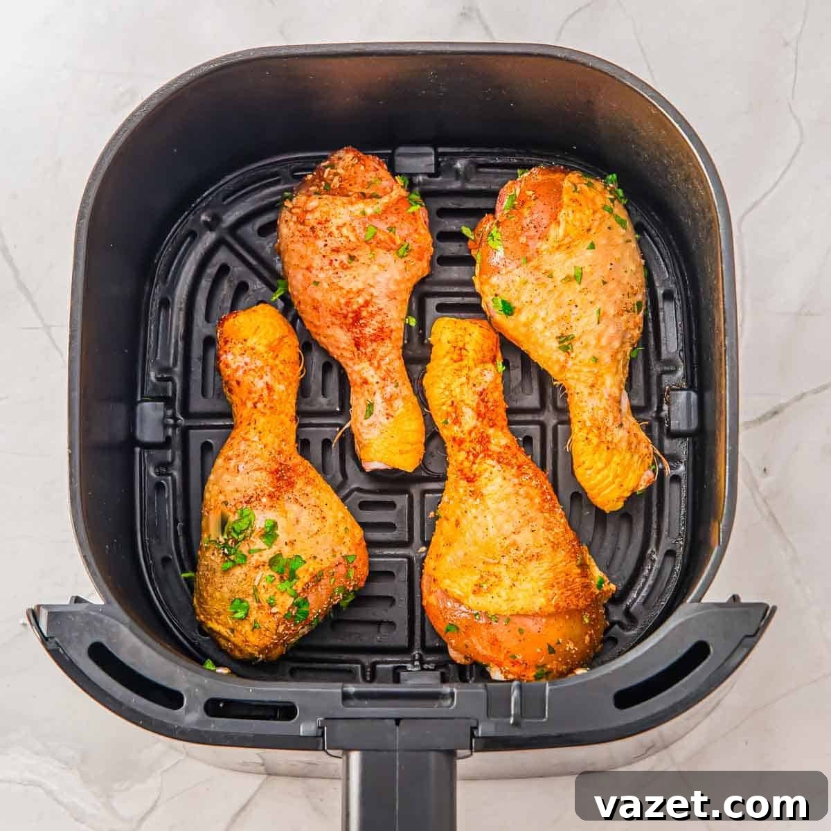 Four seasoned chicken drumsticks arranged in a single layer inside an air fryer basket on a light-colored countertop.