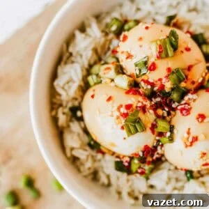 A bowl of white rice topped with three soy sauce marinated eggs, garnished with chopped green onions, red chili flakes, and sesame seeds.
