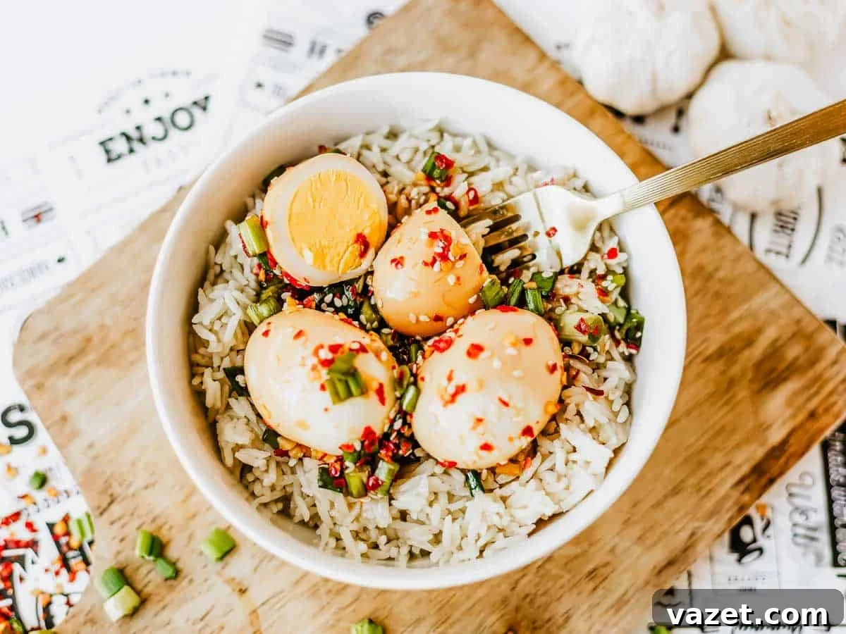 A bowl of rice topped with three Korean marinated eggs, sliced green onions, and red chili flakes, with a fork resting on the side, placed on a wooden board.