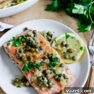 Lemon Butter Salmon Piccata with Capers and Parsley 11 Salmon piccata on a white plate with a lemon slice.
