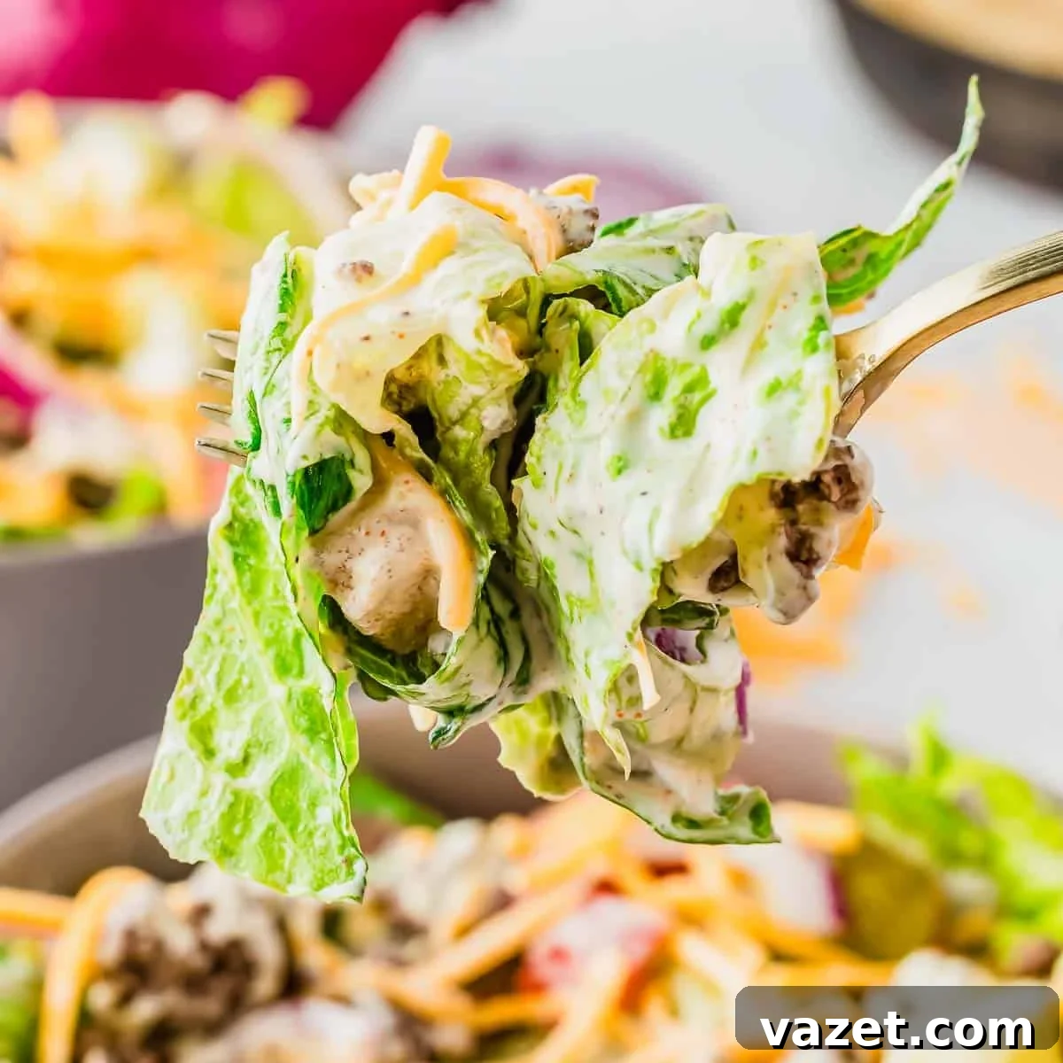 Big Mac Salad Recipe: Classic Cheeseburger Salad with Secret Sauce 12 A close-up of a fork holding a bite of salad with leafy greens, ground beef, shredded cheddar cheese, and creamy dressing. The background shows more salad in a bowl.