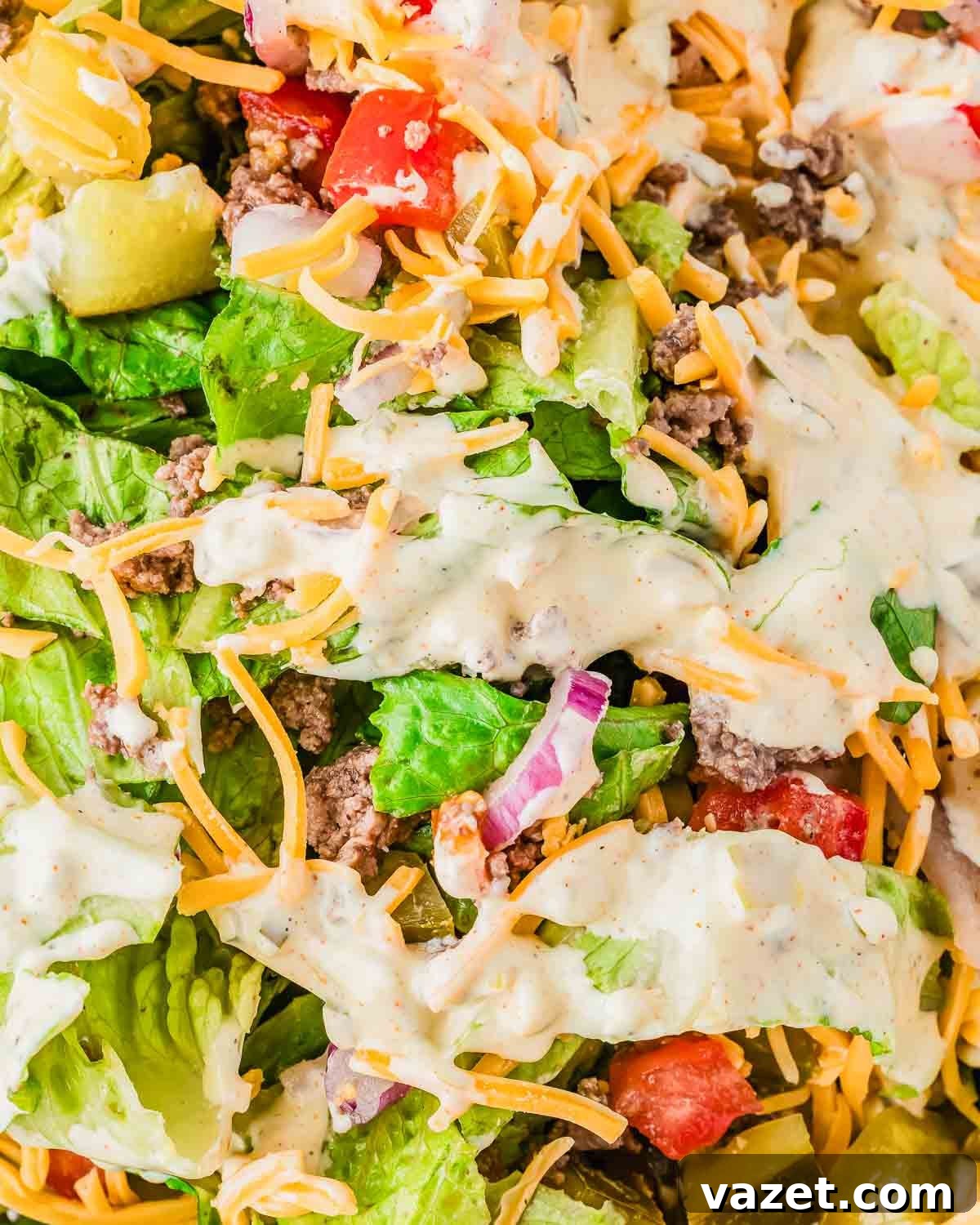 Big Mac Salad Recipe: Classic Cheeseburger Salad with Secret Sauce 3 A close-up of a fresh Big Mac salad with chopped lettuce, diced tomatoes, shredded cheddar cheese, ground beef, red onions, pickles, and a creamy dressing drizzled on top.