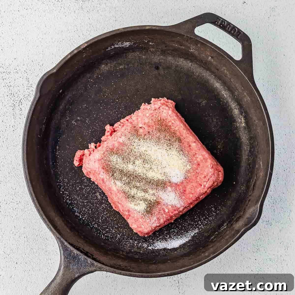 Big Mac Salad Recipe: Classic Cheeseburger Salad with Secret Sauce 7 A square portion of raw ground beef with salt and pepper sprinkled on top sits in a black cast iron skillet on a light gray surface.