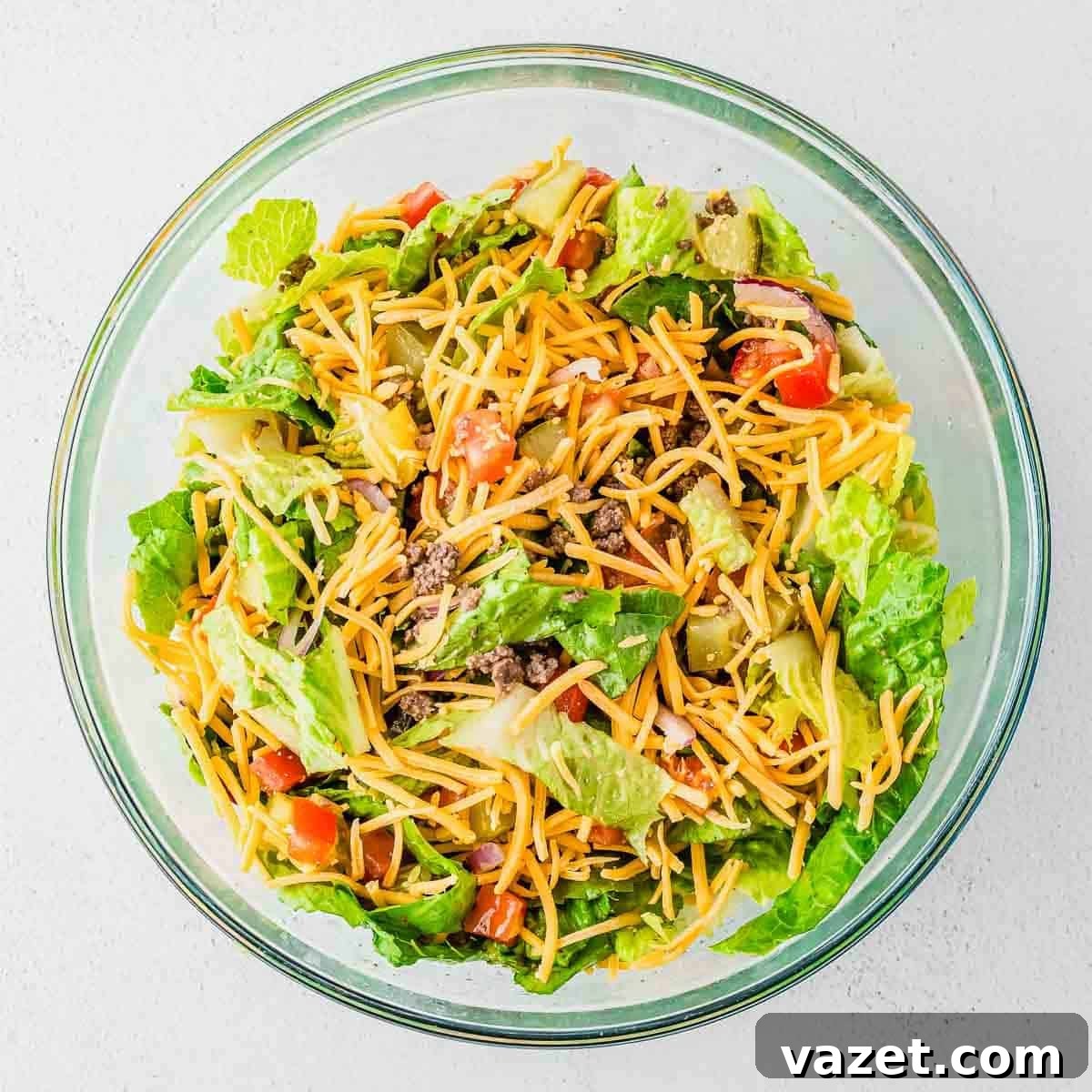 Big Mac Salad Recipe: Classic Cheeseburger Salad with Secret Sauce 10 A glass bowl filled with a colorful Big Mac burger salad containing lettuce, ground beef, shredded cheese, diced tomatoes, and tortilla chips.