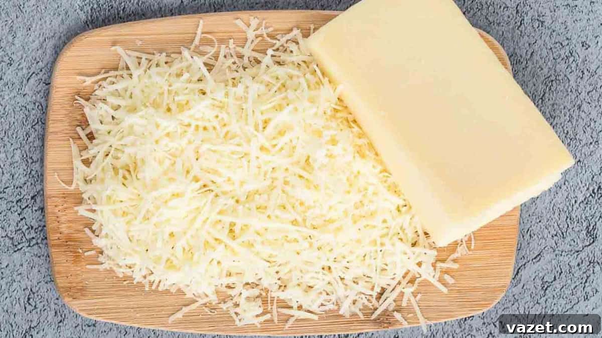 A wooden board with a block of cheese and a pile of shredded cheese on a textured gray surface.