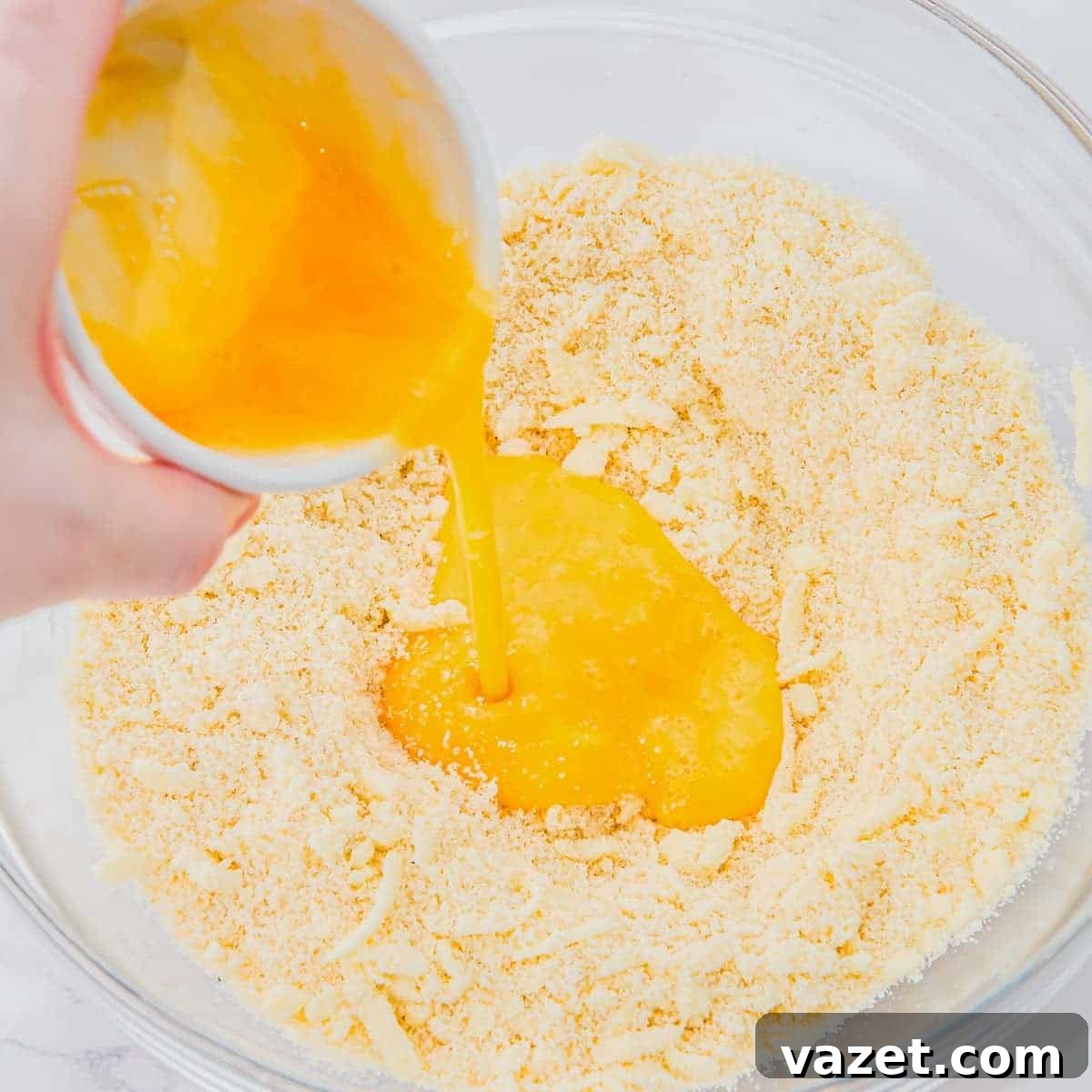 Classic Blueberry Cobbler Recipe with Cinnamon Crumble 8 A hand pours beaten eggs from a small bowl into a large glass bowl filled with a crumbly flour mixture, preparing to mix ingredients for baking.