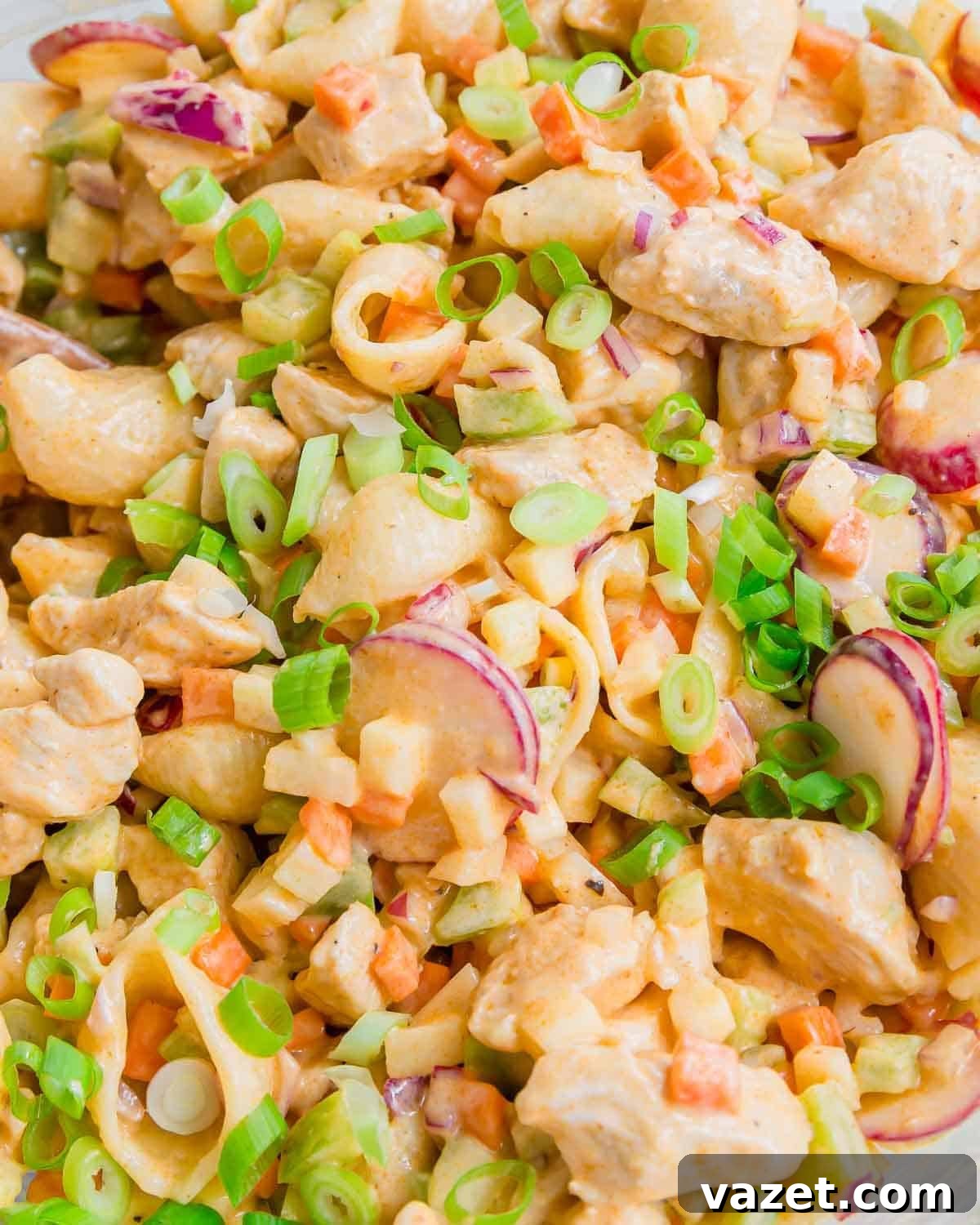 Spicy Buffalo Chicken Pasta Salad with Creamy Ranch 3 A close-up of a creamy buffalo chicken salad with cooked pasta shells, diced vegetables, radish slices, and chopped green onions sprinkled on top. The salad appears fresh and colorful.