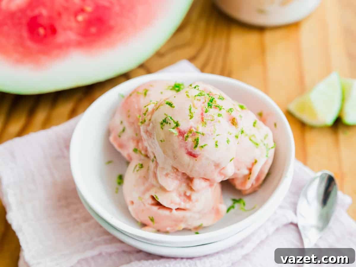 Creamy Watermelon Ice Cream Recipe 5 Three scoops of watermelon-flavored ice cream garnished with lime zest in a white bowl, set on a light cloth with a spoon. Watermelon and lime wedges are visible in the background.