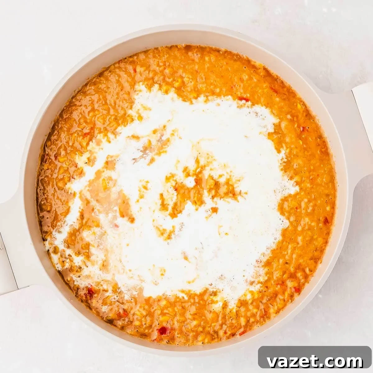 A pot of creamy street corn soup, topped with a swirl of cream, photographed from above on a light background.