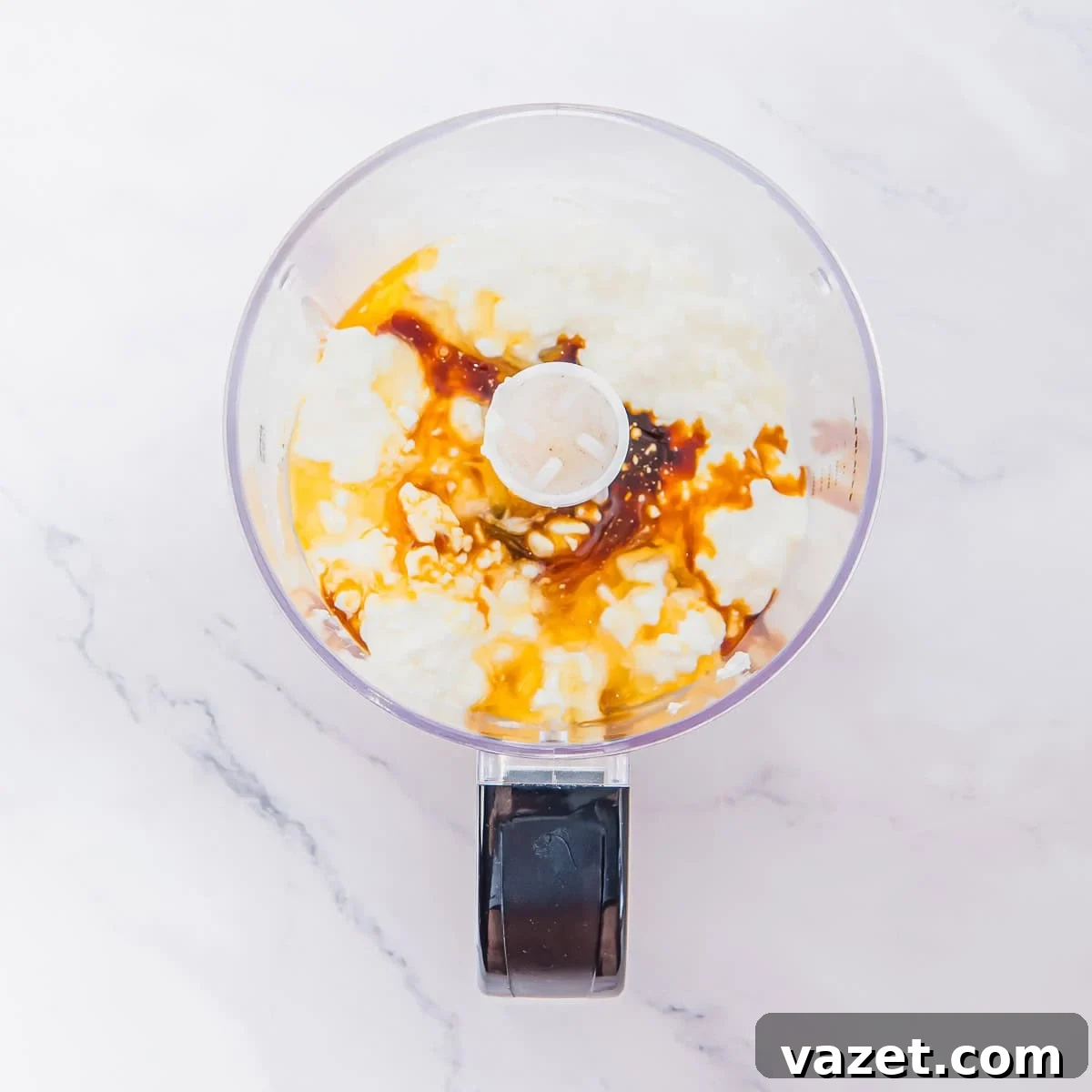 A food processor bowl holds cottage cheese ice cream ingredients on a white marble surface, ready to be blended.