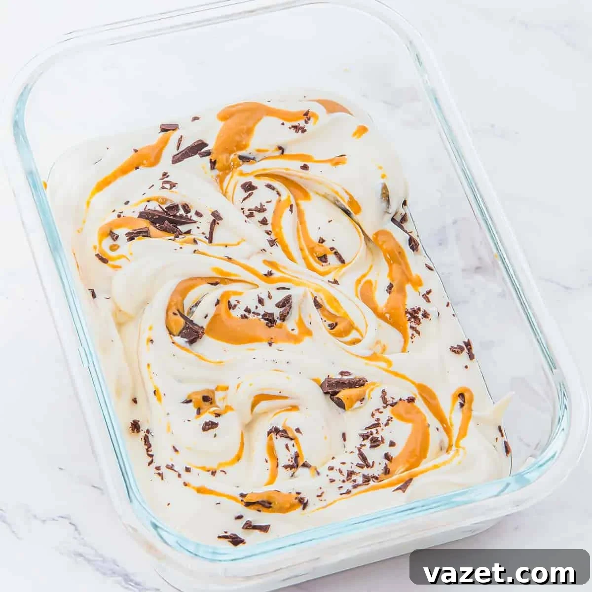 Rectangular glass dish filled with creamy white cottage cheese ice cream, swirled with peanut butter and sprinkled with chocolate shavings, on a white marble surface.